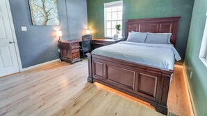 Une chambre à coucher avec un grand lit, un bureau avec une lampe, une chaise et une fenêtre.