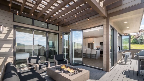 Una terrazza esterna moderna con un braciere, porte vetrate che conducono a una cucina e un patio con posti a sedere.