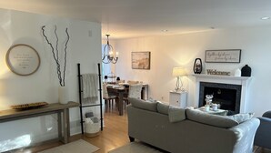 En moderne stue med en grå sofa, pejs og et spiseområde med en lysekrone.