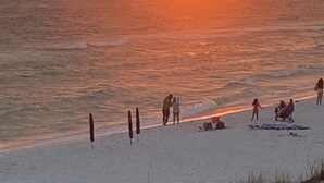 Une scène de plage où l’on voit des gens se promener et s’asseoir sur le sable, tandis que le soleil se couche sur l’océan.