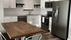 Une cuisine moderne avec des meubles blancs, une table à manger en bois et un réfrigérateur en acier inoxydable.