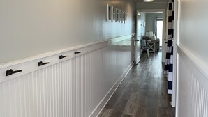 Un couloir avec des lambris blancs, un plancher en bois et un ventilateur de plafond.