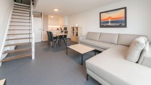 Ein modernes Wohnzimmer mit Sofa, Couchtisch und einer Treppe, die in einen Essbereich führt.