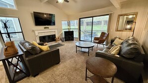 Ein geräumiges Wohnzimmer mit Kamin, Ledersofas, einem Couchtisch und einem an der Wand befestigten Fernseher.