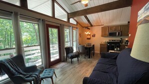 Ein geräumiges Wohnzimmer mit großem Fenster, Essbereich und Küche mit Holzausstattung und Mikrowelle.