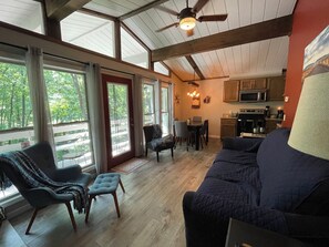Ein geräumiges Wohnzimmer mit großem Fenster, Essbereich und Küche mit Holzausstattung und Mikrowelle.