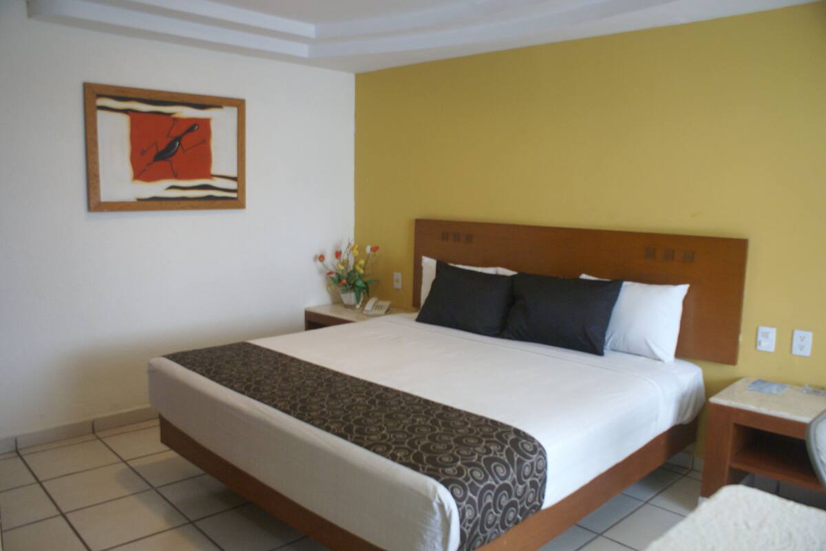 A hotel room with a large bed, a nightstand with a vase of flowers, and a painting on the wall.