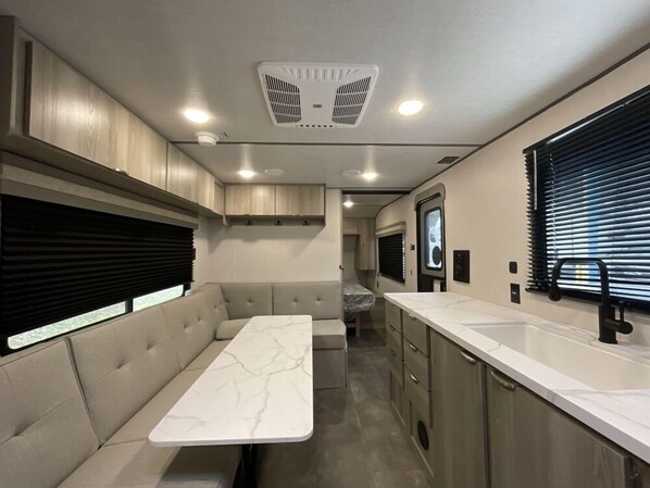 Compact kitchenette with a long countertop, cushioned bench, and small window for natural light.