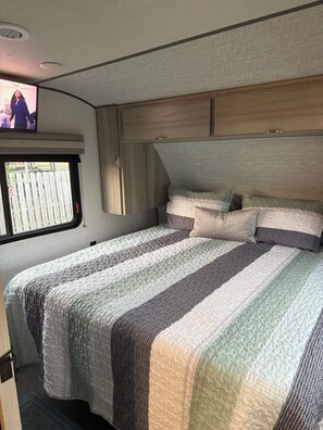 Relax in this RV with a comfortable bed, TV, and a view of a residential area.