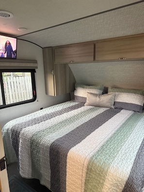 Relax in this RV with a comfortable bed, TV, and a view of a residential area.