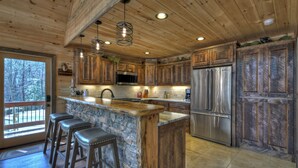 Una cocina con armarios de madera, una isla de piedra, electrodomésticos de acero inoxidable y una zona de asientos con taburetes de bar.