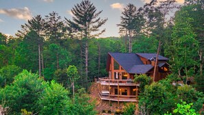 Una cabaña con terraza, rodeada de un bosque frondoso.
