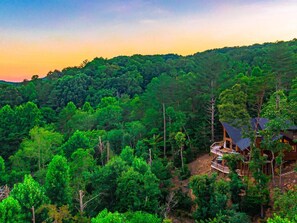 A forested landscape with a cabin-style building featuring multiple levels and a prominent staircase.
