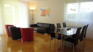 Un salon moderne avec un canapé, des fauteuils rouges, une table à manger avec des chaises et un tableau accroché au mur.