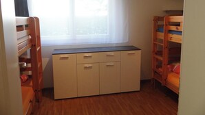 Une chambre avec des lits superposés, une fenêtre avec des rideaux légers et un bureau intégré avec des rangements.