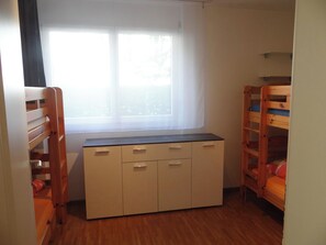 Ein Zimmer mit Etagenbetten, einem Fenster mit durchscheinenden Vorhängen und einem eingebauten Schreibtisch mit Stauraum.