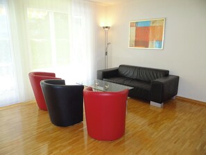 A modern living room with a glass coffee table, a black leather sofa, and two red cylindrical stools.