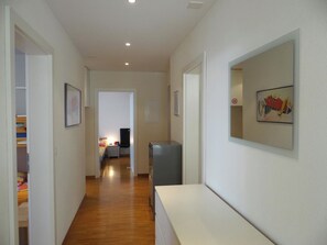 A hallway with a bed, a desk, and a refrigerator. There are framed pictures on the walls.