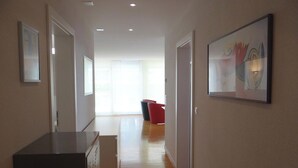 Un couloir avec un plancher en bois, une armoire noire et, au fond, une chaise rouge.
