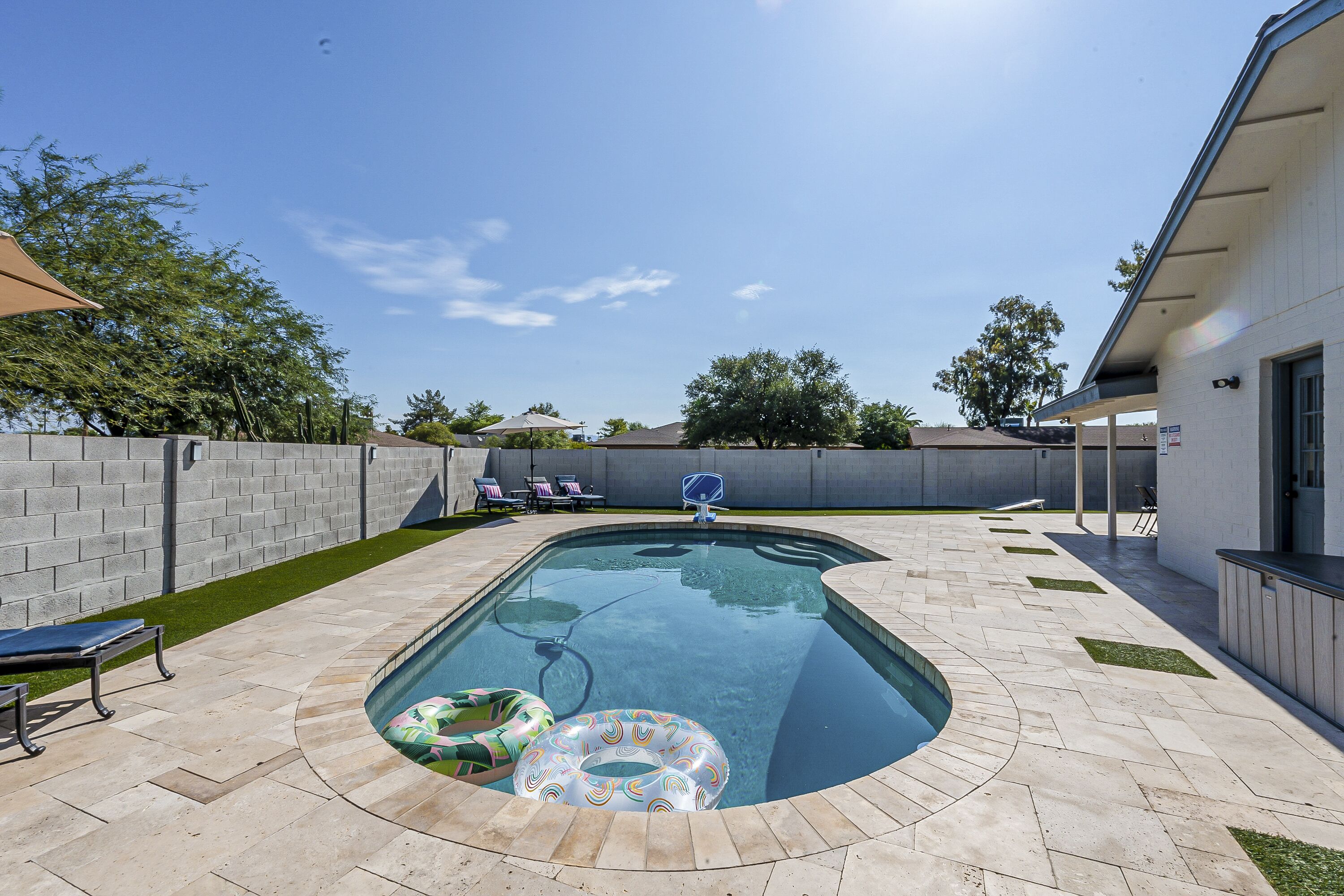 Ein Schwimmbecken mit Basketballkorb, Liegestühlen und einer überdachten Terrasse.