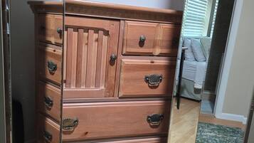 A wooden dresser with multiple drawers and knobs, positioned in a room with a wooden floor and a mirror reflecting part of the room.