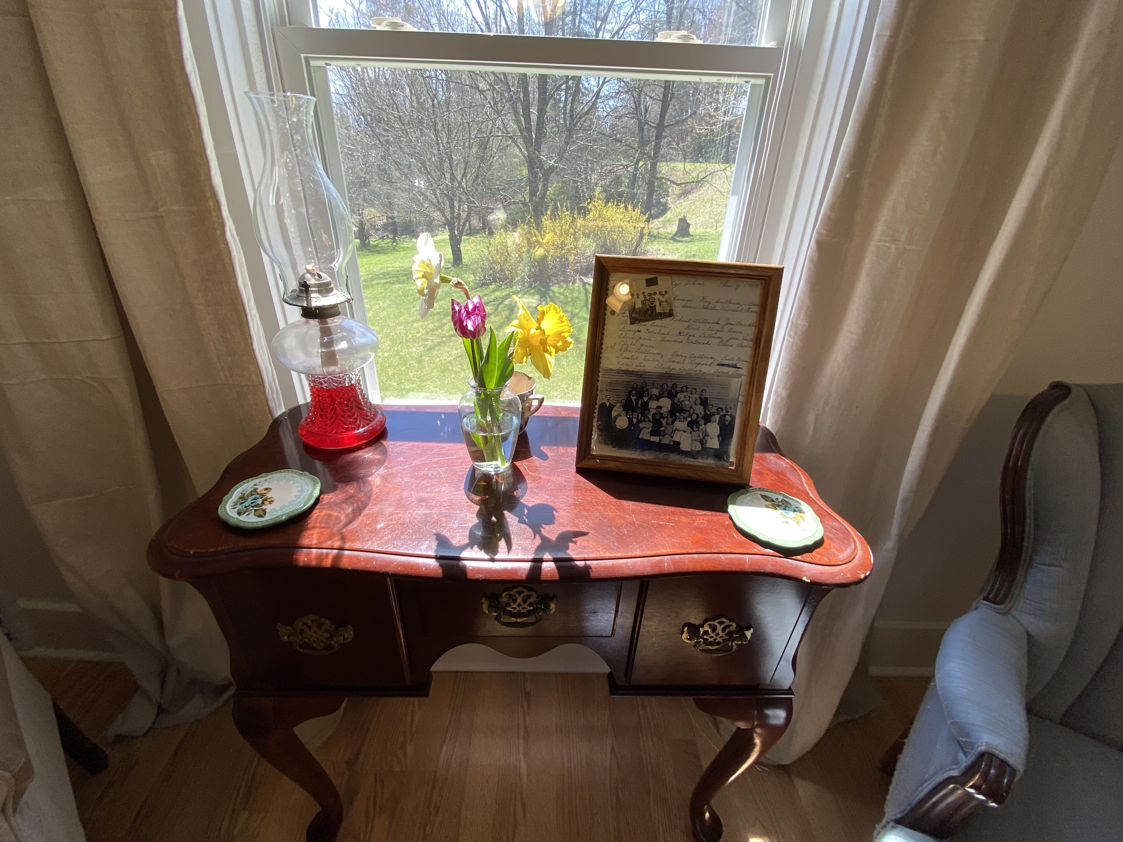 Ein Holztisch mit einem gerahmten Foto, einer Vase mit Blumen und einer roten Lampe.