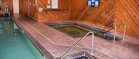 A wooden-paneled indoor pool with a hot tub, tiled steps, and a metal ladder.