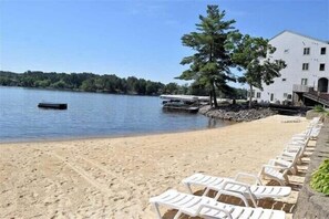 A beach with white lounge chairs and a white building with a balcony.