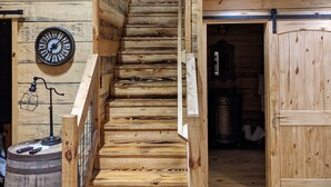 A wooden staircase in a rustic cabin with a clock on the wall and a barrel at the bottom. - Faye's Retreat (Fort Payne)