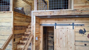 A rustic wooden cabin with a staircase leading to a loft area, a door with a rooster decal, and a small kitchen area. - Faye's Retreat (Fort Payne)