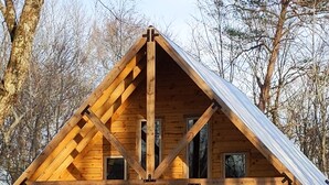 A wooden cabin with a gabled roof, a front porch with steps, and a fenced area. - Faye's Retreat (Fort Payne)