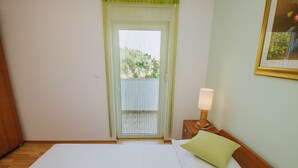 Une chambre avec un lit, une table de chevet avec une lampe, une fenêtre donnant sur un paysage verdoyant et un tableau encadré au mur.