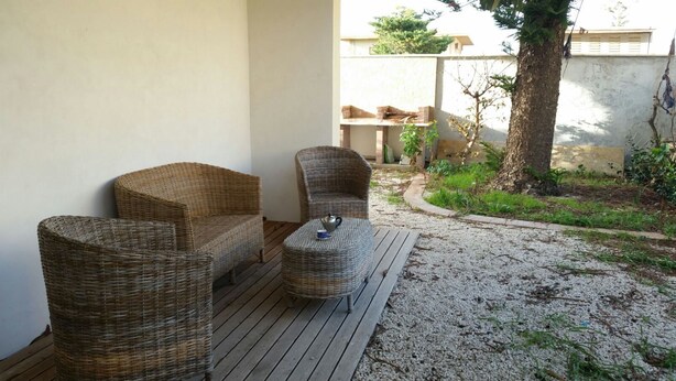 Een terras met rieten meubels en een kleine tafel, omgeven door een grindpad en groen.