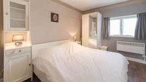 A bedroom with a large bed, a bedside table with a lamp, a wardrobe, a mirror, and a window with curtains. - Orchidee 002 - cozy app on ground floor by Interhome (De Haan)