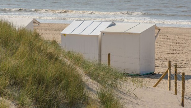 A beach with a small white building, possibly a lifeguard hut, and a sailboat in the distance. - Orchidee 002 - cozy app on ground floor by Interhome (De Haan)