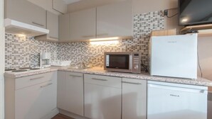 A compact kitchen with white cabinets, a microwave, a refrigerator, and a tiled backsplash. - Orchidee 002 - cozy app on ground floor by Interhome (De Haan)
