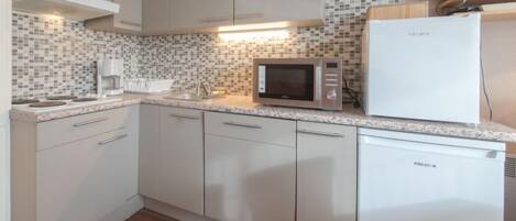 A compact kitchen with white cabinets, a microwave, a refrigerator, and a tiled backsplash.