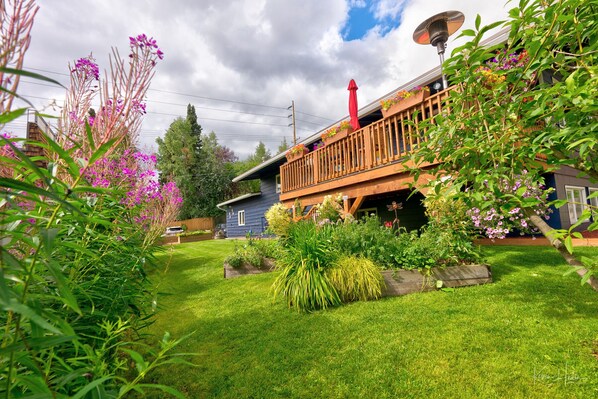A house with a wooden deck, a satellite dish, and a garden with various plants and flowers.