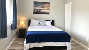A bedroom with a bed, a nightstand, a lamp, a painting on the wall, and a window with curtains. - Central Frisco-Full renovated cozy&nice half duplex 3bed|2bath free wifi&parking (Frisco)