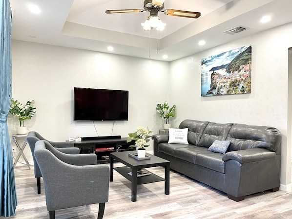 A modern living room with a flat-screen TV, a leather sofa, a coffee table, and a ceiling fan.
