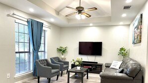 A modern living room with a flat-screen TV, grey armchairs, a leather sofa, a coffee table, and a ceiling fan. - Central Frisco-Full renovated cozy&nice half duplex 3bed|2bath free wifi&parking (Frisco)