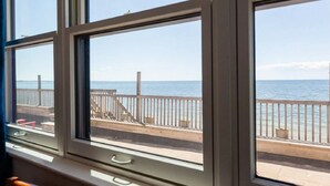 A view from a window overlooking a wooden deck with a railing, leading to a beach. - Unwind at the Scallop Saturday cottage located at the Oceana Cottages (North Truro)