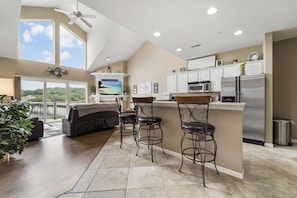 A modern kitchen with a large island, bar stools, and a view of the outdoors.