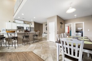 A spacious kitchen with white cabinets, a dining area with a large table and chairs, and a view of the living room.