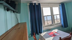 A room with a wooden table, two chairs, a TV mounted on the wall, and a window with curtains.