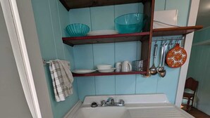 A compact kitchen with a white sink, a wooden shelf above, and a blue wall.