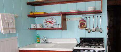 A kitchen with wooden cabinets, a white stove, and shelves holding dishes and utensils.