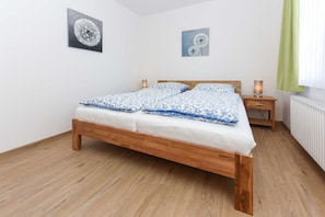 Une chambre à coucher avec un lit en bois, deux tableaux accrochés au mur, une table de chevet avec une lampe et un radiateur.