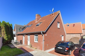Une maison en briques rouges, avec un toit en pente, une antenne parabolique et une voiture garée dans l’allée.