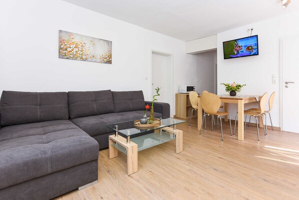 Un salon moderne avec un canapé gris, une table basse en verre et un coin repas comprenant une table et des chaises en bois.